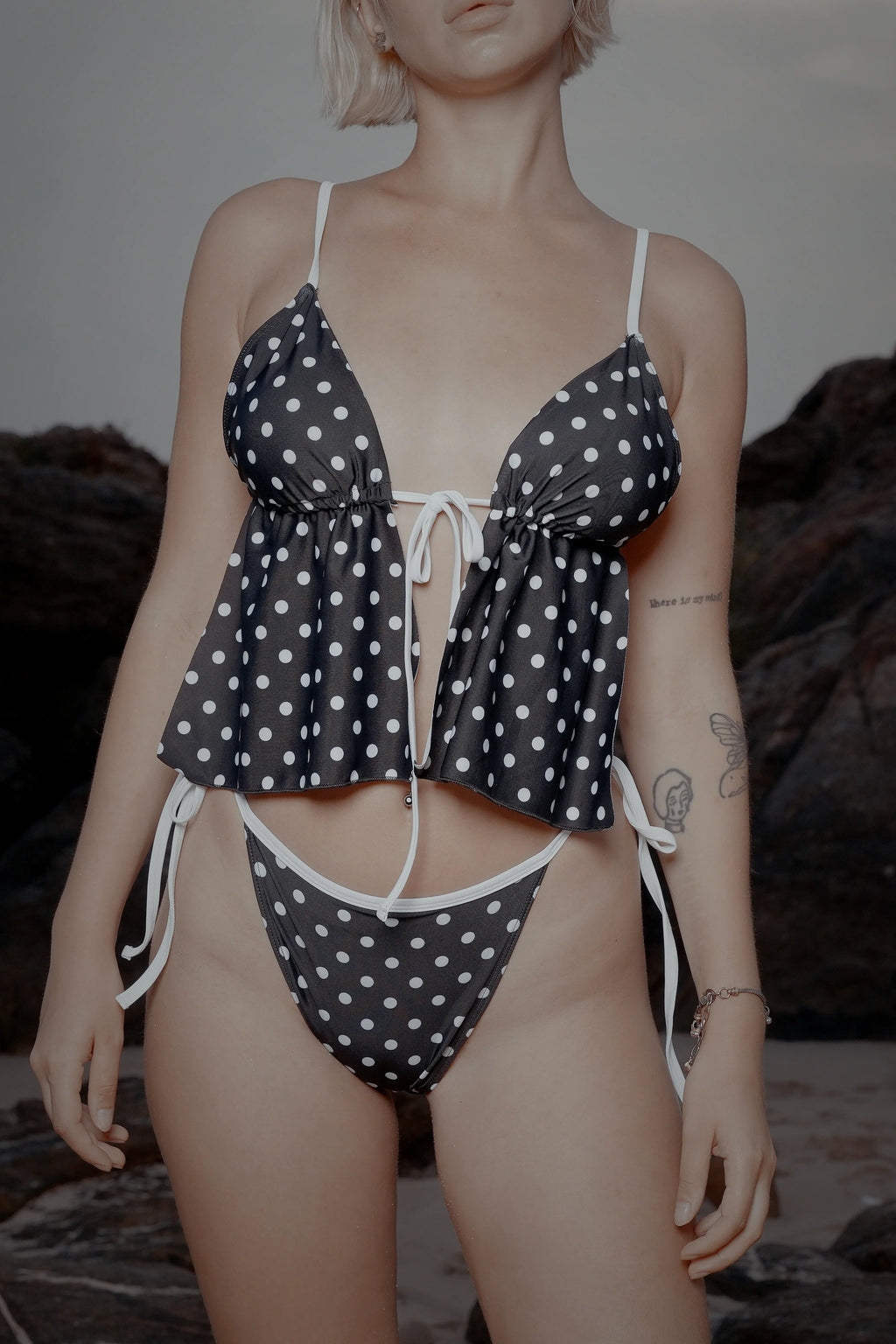Woman wearing a black and white polka dot bikini beachwear, beach rocks in background